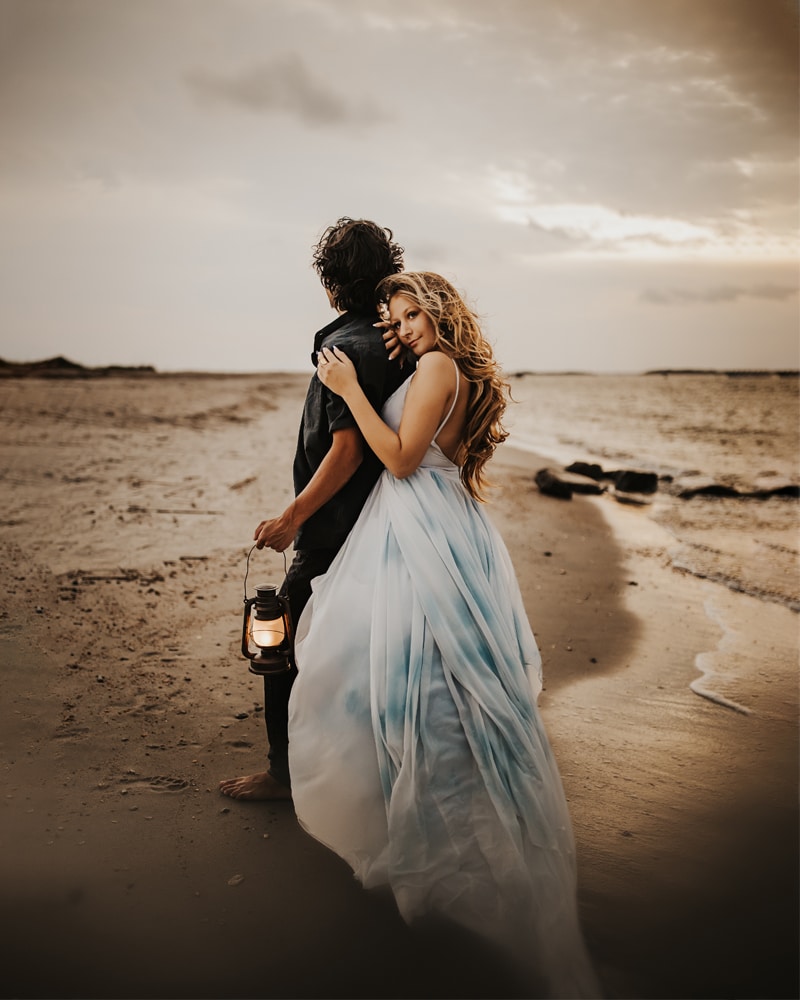 Family Photographer, a woman embraces her husband on the beach, she wears a blue dress
